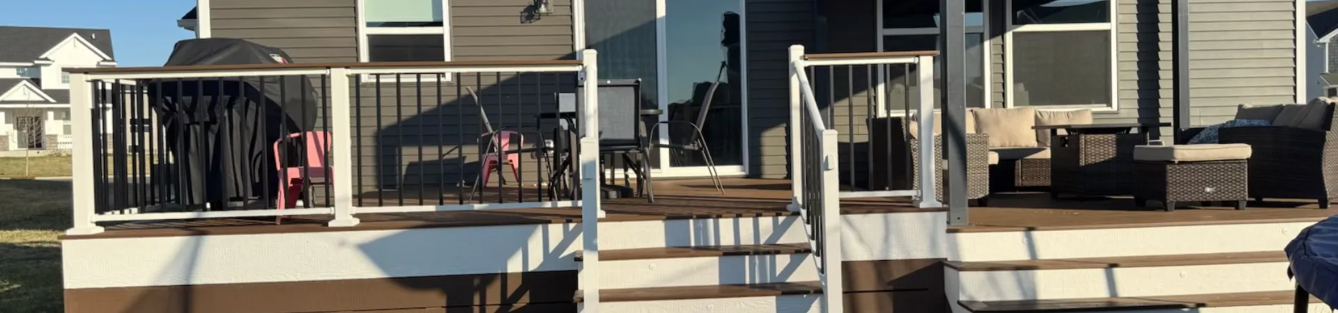 Completed composite deck project in Carver with a covered outdoor living space, wide stairs, and black railings