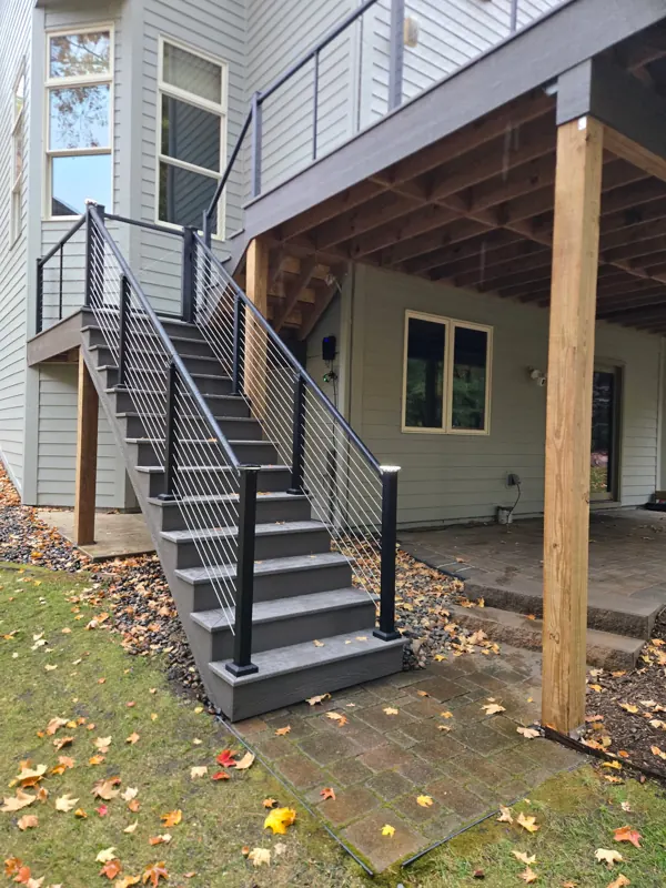 Elevated gray deck and staircase with black cable railings beside the house