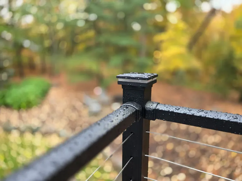 Close view of a black railing post, top rail, and horizontal cables