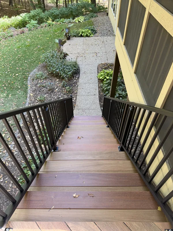 View down the brown deck stairs toward the landscaped yard