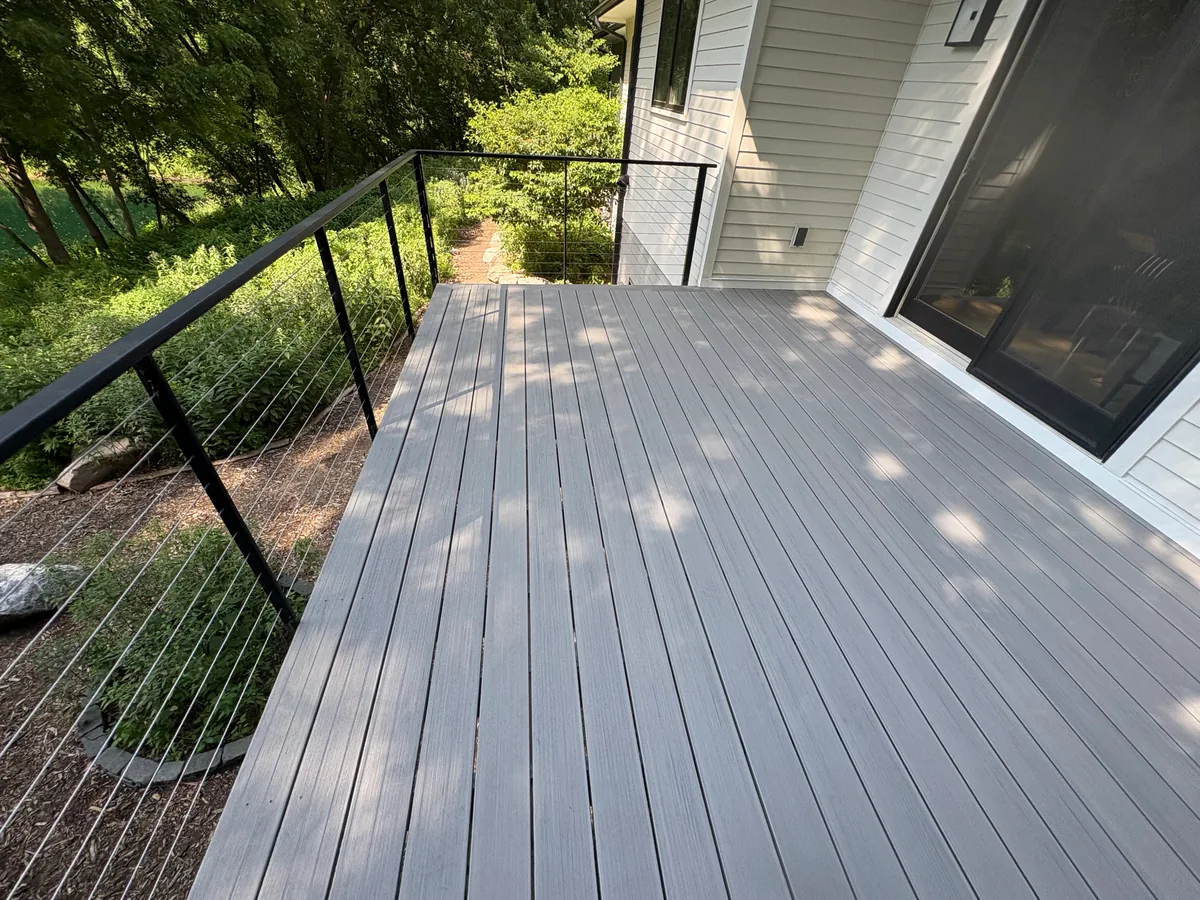 Finished Hopkins composite deck platform with black cable railing overlooking wooded landscaping