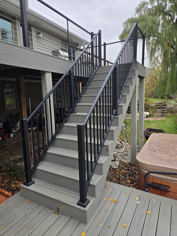 Gray deck stairs with black vertical balusters connecting the upper deck and lower landing