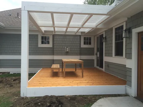 White pergola over a wood deck patio attached to the home