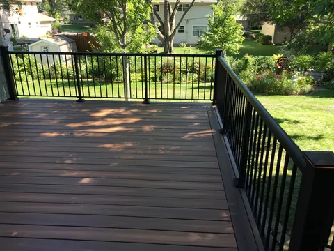 Composite deck surface with black railing overlooking a landscaped backyard